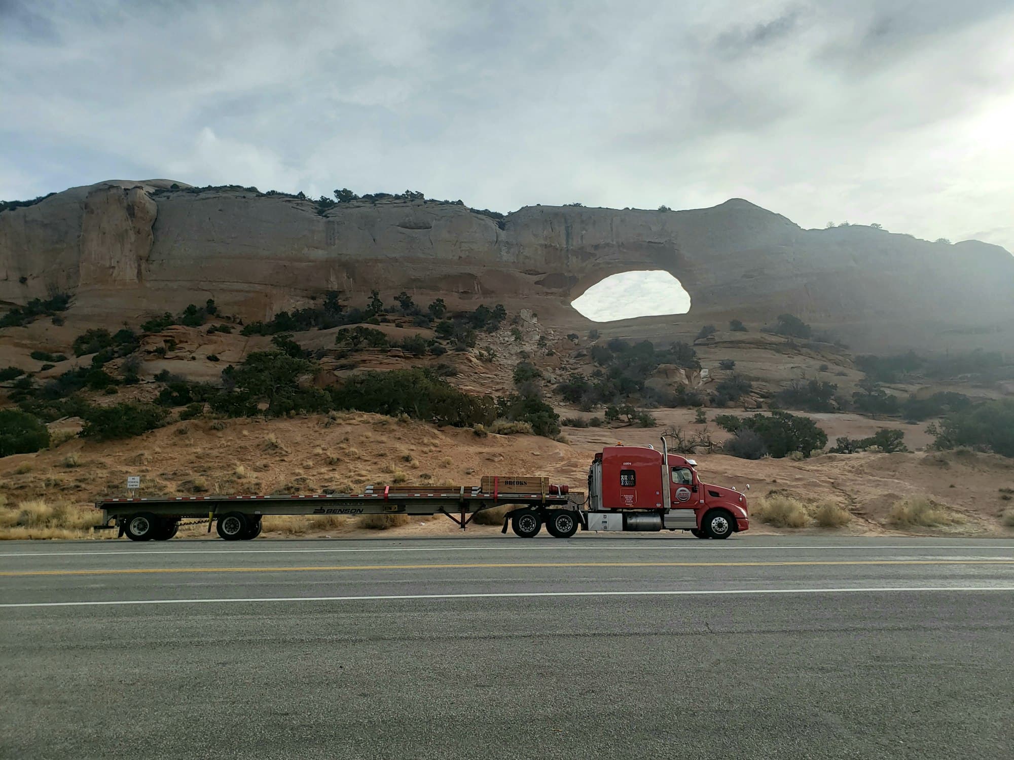 Красный тягач Peterbilt с открытой платформой flatbed у скальной арки в Юте